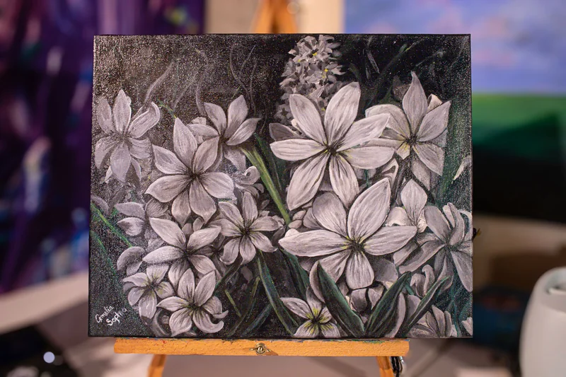 An acrylic painting of white star-shaped flowers on a dark background, standing on a wooden easel.